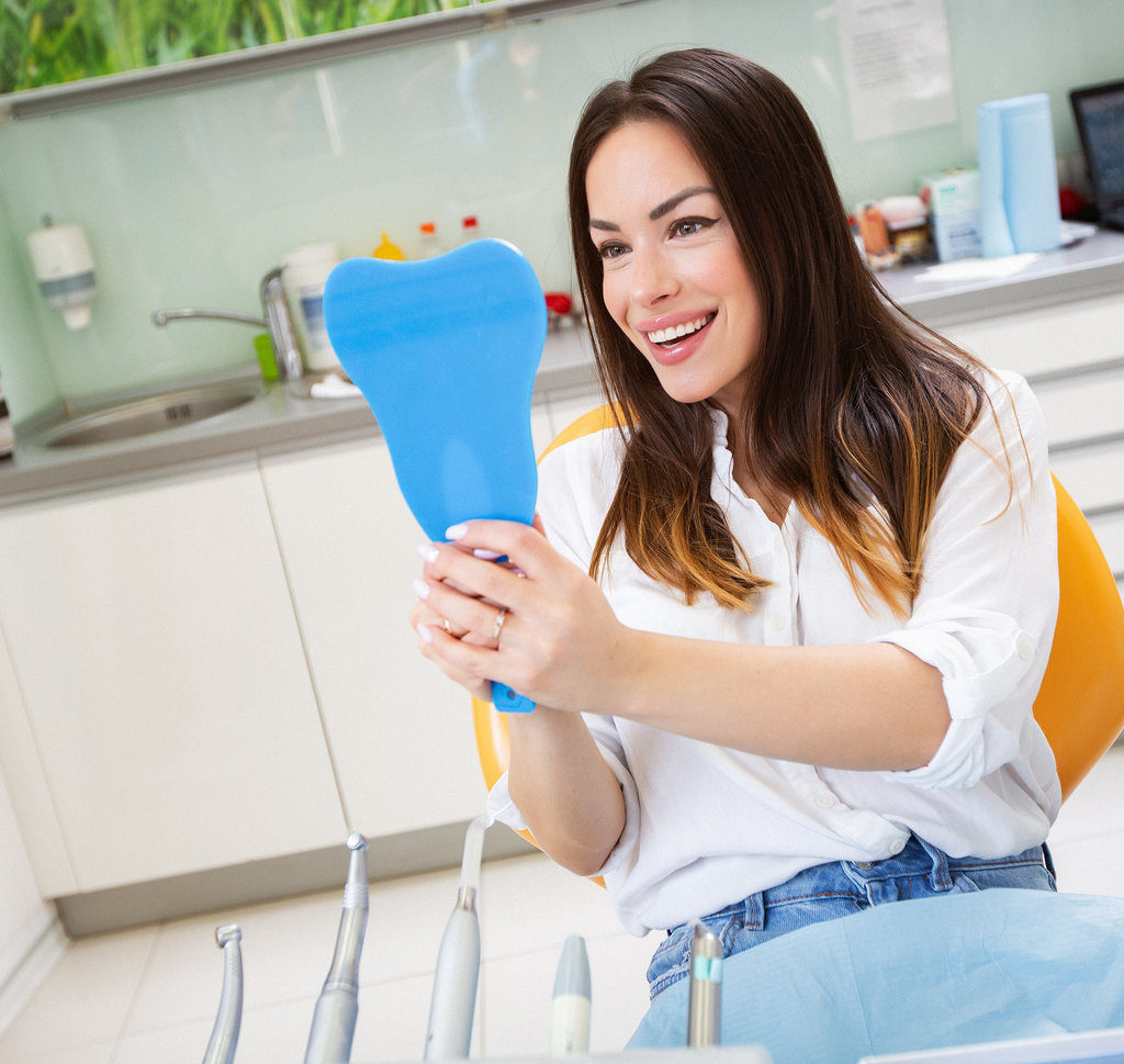 Beautiful young woman checking teeth in mirror