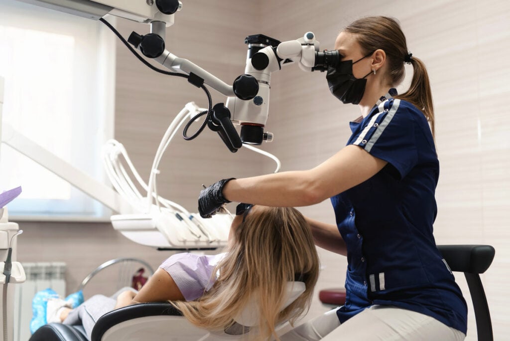 Doctor making teeth examination research survey using microscope in dentistry. Dentist is treating patient in modern dental office.